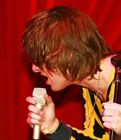 side profile of a man singing in front of a red curtain